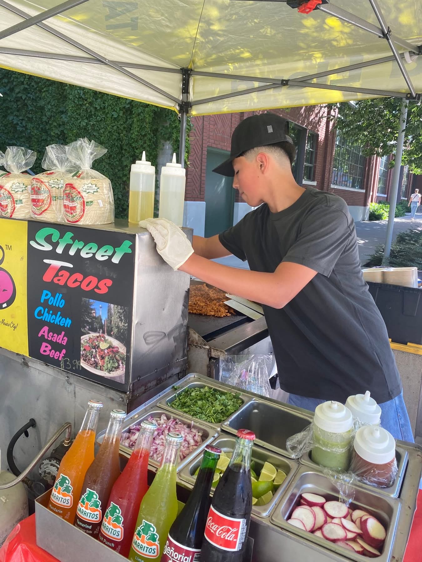 Barriga Llena vendor preparing street tacos at the griddle with the menu board and Jarritos bottles